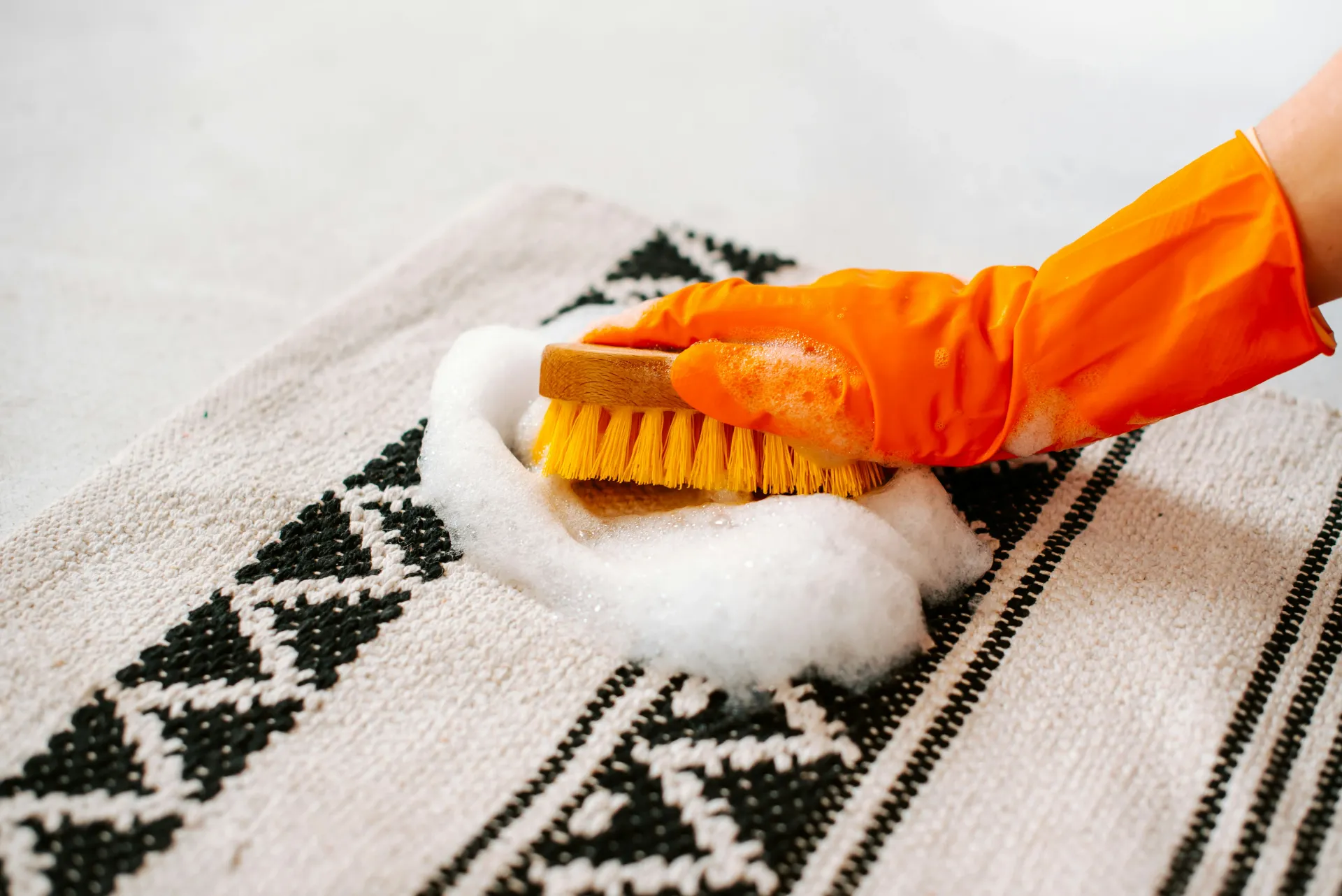 Professional carpet or upholstery cleaning in progress, showing a hand in a glove scrubbing a rug with foam.