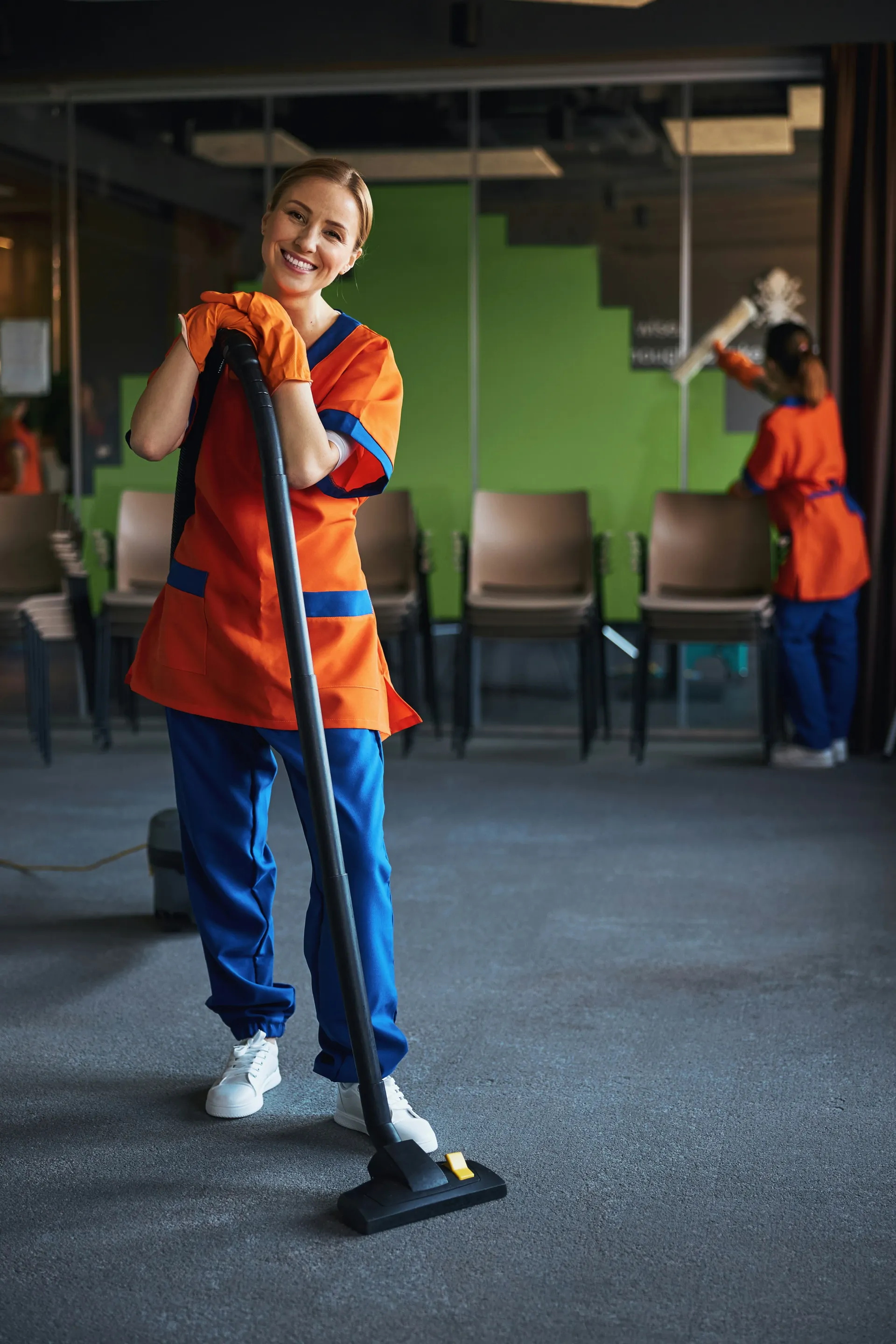 Professional cleaner smiling with a vacuum cleaner in an office or commercial building.